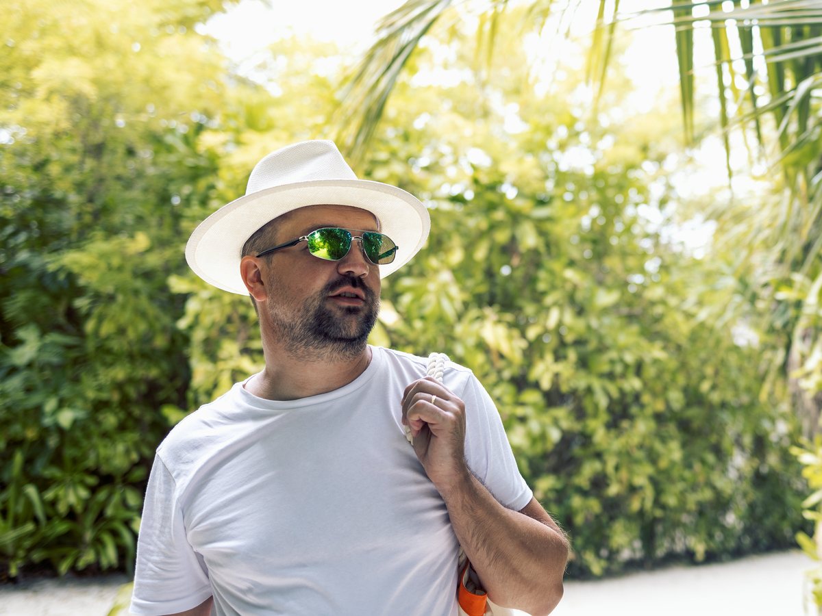 A man in a white shirt and hat walking through palm trees in Miami