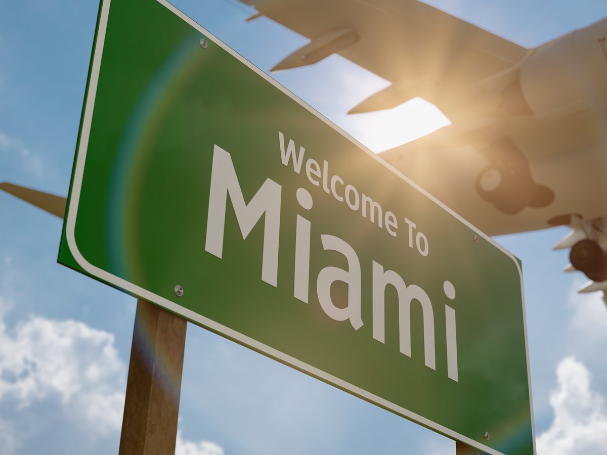 A green 'Welcome To Miami' road sign under a bright sky